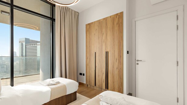 Een moderne hotelkamer met twee bedden, een groot raam, een houten garderobe en een deur.