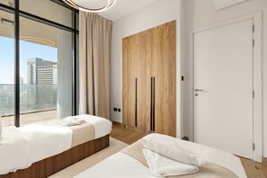 A modern hotel room with two beds, a large window, a wooden wardrobe, and a door. - Silkhaus Executive 3bdr in Maryah Island (Abu Dhabi)
