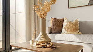Een moderne woonkamer met een houten salontafel, een vaas met gedroogde bloemen en een bank met gestructureerde kussens.