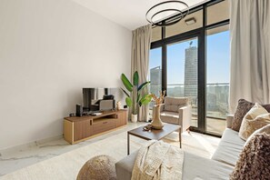 A modern living room with a TV, sofa, coffee table, and large windows with a city view. - Silkhaus Executive 3bdr in Maryah Island (Abu Dhabi)