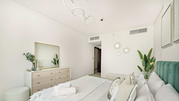 Een moderne slaapkamer met een bed, een dressoir, een spiegel en een plant.