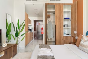 A hotel room with a bed, bedside table, a mirror, a potted plant, a wardrobe, and a closet with shelves. - Silkhaus Stylish Studio With Balcony 2 Min to Adgm in Al Maryah Vista (Abu Dhabi)