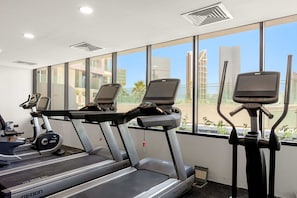 Ein Fitnessstudio mit Laufbändern und einem Crosstrainer, großen Fenstern mit Blick auf die Stadt und einer Decke mit Einbautenbeleuchtung.
