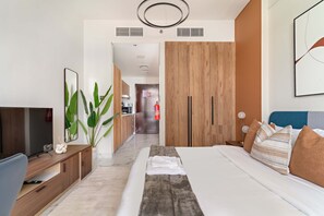 Ein modernes Hotelzimmer mit Bett, Fernseher, Schreibtisch und einer großen Pflanze.