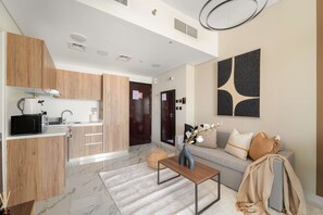 A modern living room with a sofa, a coffee table, and a kitchen area with wooden cabinets and a microwave. - Silkhaus Upscale 1BR in Maryah Island Nearby Canal (Abu Dhabi)