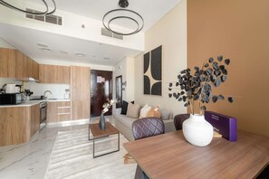 A modern kitchen with a built-in oven, a dining area with a wooden table, and a living room with a sofa and decorative wall art. - Silkhaus Upscale 1BR in Maryah Island Nearby Canal (Abu Dhabi)