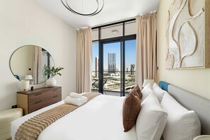 Habitación de hotel con una cama grande, cómoda, un espejo y vistas a un paisaje urbano a través de amplias ventanas.