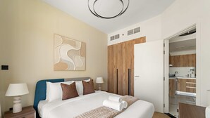 Ein modernes Hotelzimmer mit einem großen Bett, einem Holzschrank, einer Küchenzeile und einem durch eine offene Tür einsehbaren Badezimmer.