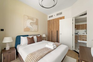 A modern hotel room with a large bed, a wooden wardrobe, a kitchenette, and a bathroom visible through an open door. - Silkhaus Chic 1BR in Maryah Vista Maryah Island (Abu Dhabi)