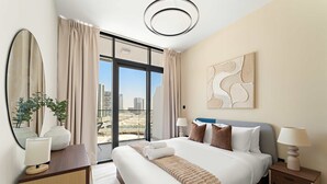Ein Hotelzimmer mit einem großen Bett, einem Schreibtisch mit Lampe, einem Spiegel und Blick auf die Stadt.