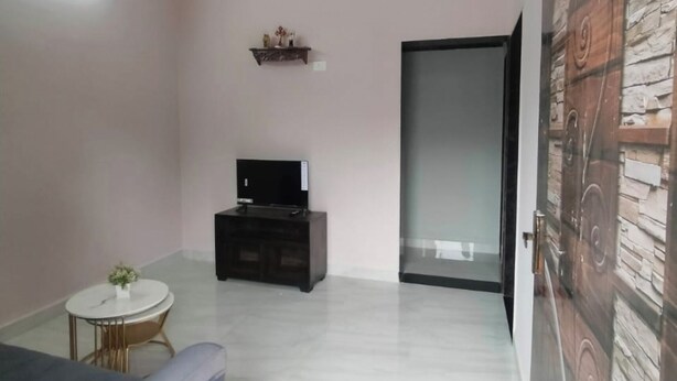 Una sala de estar moderna con un televisor de pantalla plana sobre un soporte negro, una mesita redonda con una planta y un ventanal corredizo que da a un muro de piedra.
