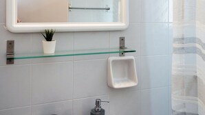Un bagno con un lavandino bianco, uno scaffale in vetro con una pianta in vaso, uno specchio e una tenda da doccia.