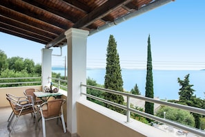 A balcony with a table and chairs, overlooking a body of water and greenery.
