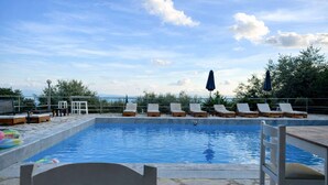 A swimming pool with lounge chairs and umbrellas, surrounded by stone tiles and greenery. - Hotel Barbati - Pool & Panoramic Sea View Escape (Corfu)