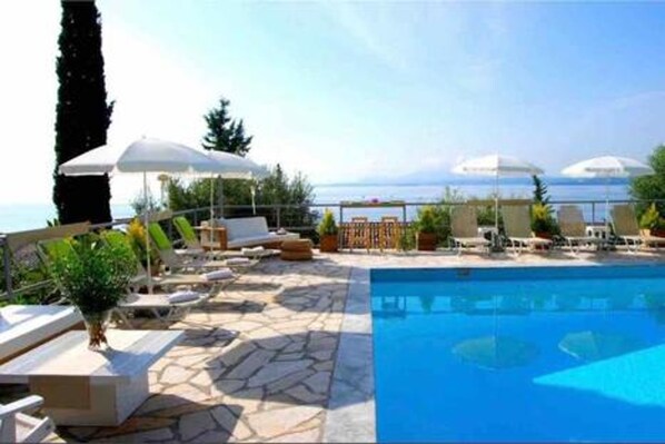 A poolside area with lounge chairs and umbrellas, a stone-tiled deck, and a view of the sea. - Hotel Barbati - Poolside Gem With Sea Views (Corfu)