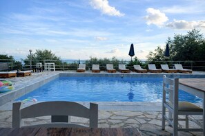 A swimming pool with lounge chairs and umbrellas, surrounded by stone tiles and greenery. - Hotel Barbati - Poolside Gem With Sea Views (Corfu)