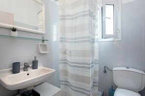 Un baño con un lavamanos blanco, un espejo, una estantería de vidrio con una planta en maceta, una cortina de ducha a rayas y un inodoro.