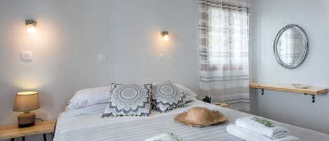 Een netjes ingerichte slaapkamer met een bed, kussens, een bedlampje, een spiegel en handdoeken op het bed.