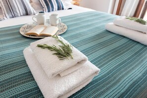 Una cama bien hecha con una colcha azul a rayas, una pila de toallas blancas y un libro sobre un plato junto a una taza y un platillo.