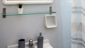 A bathroom with a white sink, a glass shelf with a potted plant, a mirror, and a shower curtain. - Hotel Barbati - Sea & Mountain View Escape (Corfu)