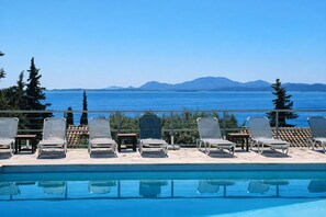 Zona de piscina con sillones de descanso y vistas al mar y a las montañas.