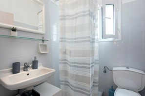 Une salle de bain avec un lavabo blanc, un miroir, une étagère en verre sur laquelle est posée une plante en pot, un rideau de douche à rayures et des toilettes.