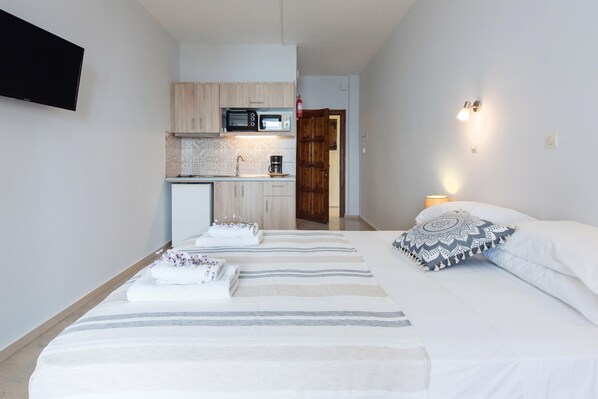 A bedroom with a bed, pillows, and a bedside table. There is a kitchen area with a microwave, coffee maker, and cabinets. - Hotel Barbati - Studio With Sea Mountain Views (Corfu)