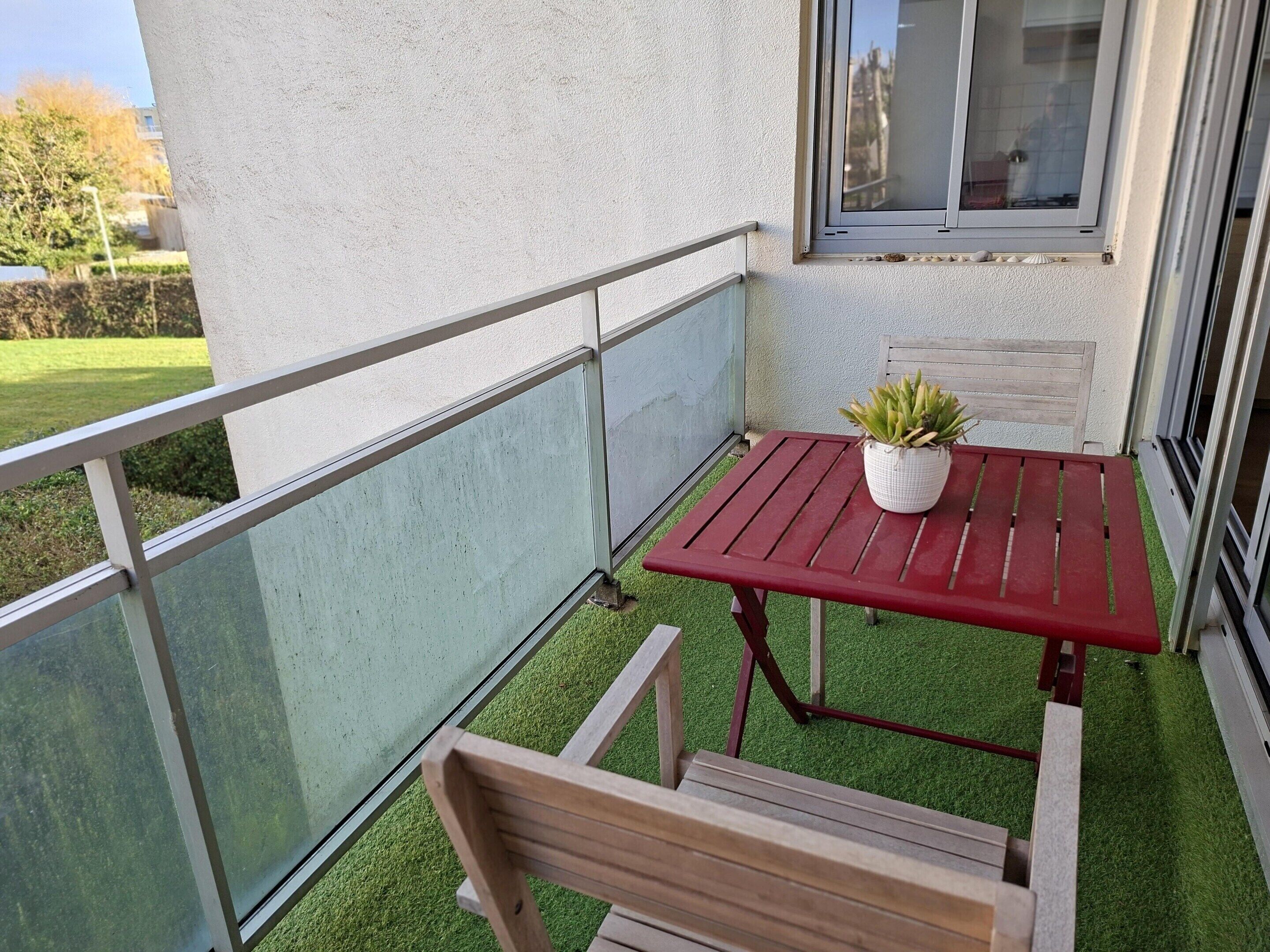 A balcony with a red table, a wooden bench, and a potted plant.