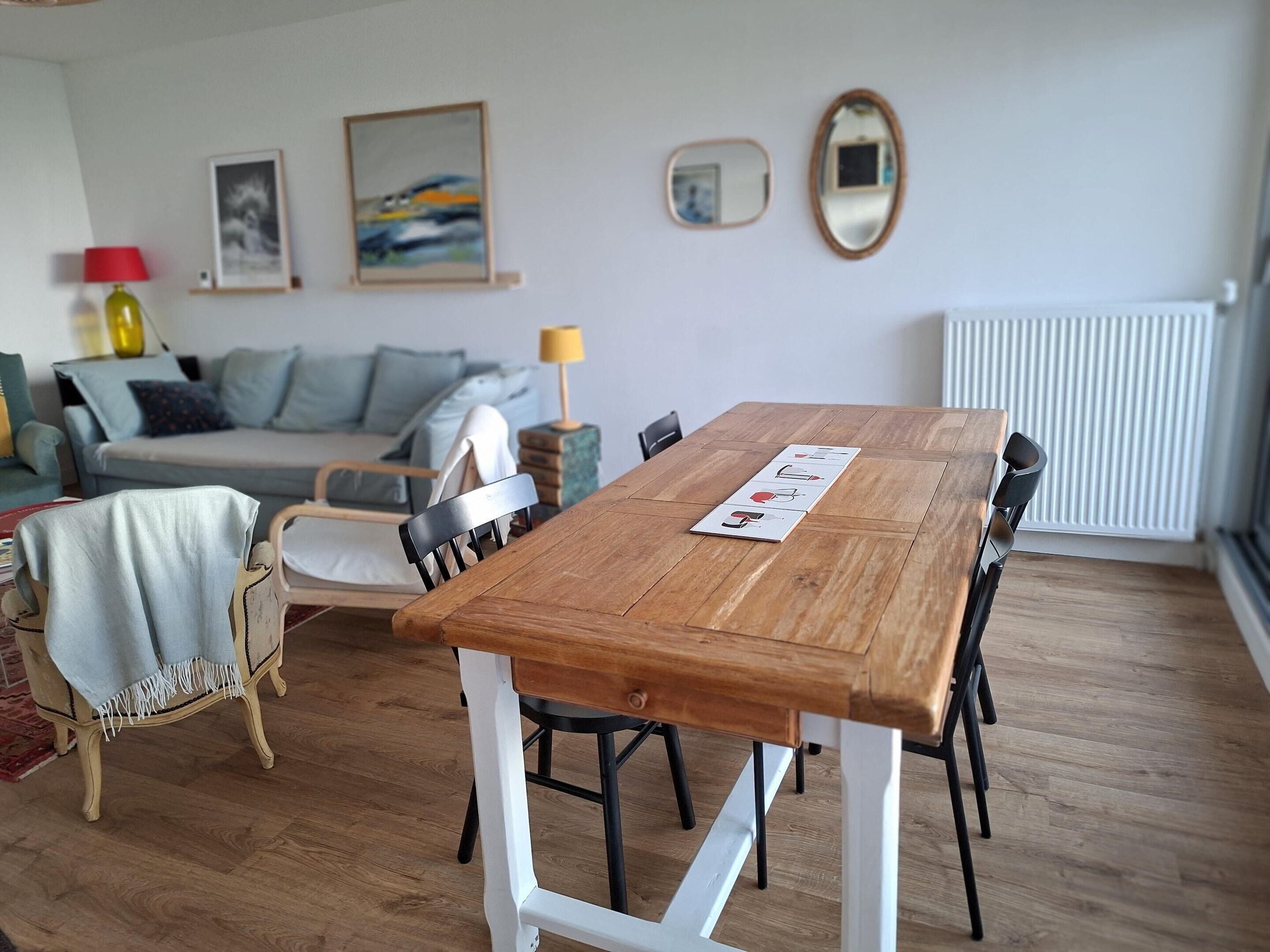 Et spiseområde med et træbord, stole og en sofa i baggrunden.