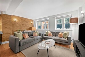 Ein modernes Wohnzimmer mit zwei grauen Sofas, einem Glastisch und einer Ziegelwand als Blickfang.