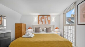 Habitación de hotel moderna con una cama grande, un armario de madera, un escritorio con una silla y una ventana con vistas a edificios.