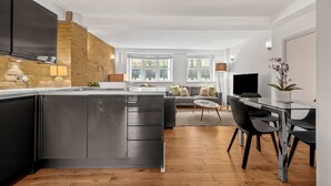 Una cocina moderna con una isla central, un comedor con mesa de vidrio y una sala de estar con sofá y televisor.