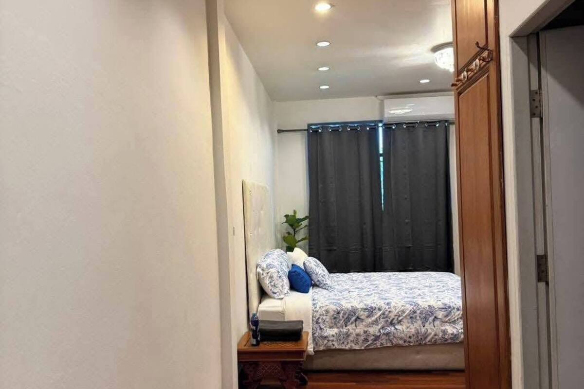 Een smalle gang met een houten vloer die leidt naar een kamer met een bed, een nachtkastje en een raam met gordijnen.