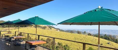 A wooden deck with outdoor seating and green umbrellas overlooking a grassy landscape.