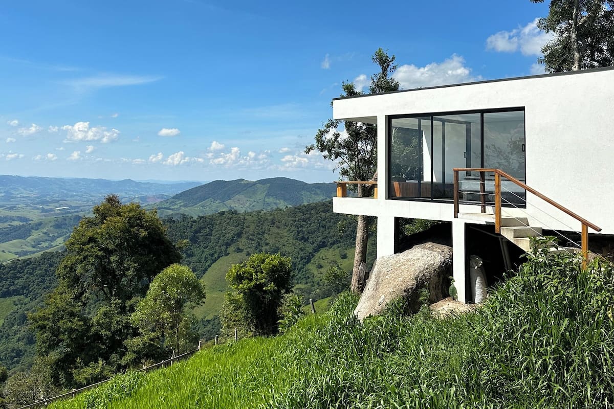 Un edificio moderno con fachada de vidrio, ubicado en una colina con vistas a un valle exuberante.
