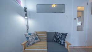 Ein kleiner, gemütlicher Raum mit einem Schlafsofa, einer Lampe und einer Tür zu einem anderen Zimmer.