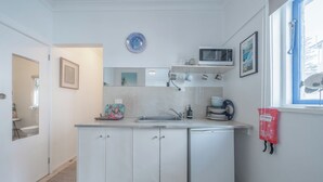 Eine kleine Küche mit weißen Schränken, einer Mikrowelle, einem Spülbecken und einem kleinen Kühlschrank.