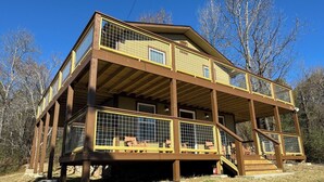 A two-story wooden cabin with a balcony, surrounded by trees.