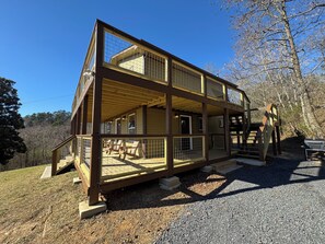 Une cabane en bois à deux étages, dotée d’un balcon et d’une terrasse, entourée d’arbres.