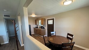 A modern kitchen with wooden cabinets, a dining area with a round table and chairs, and a door with windows.