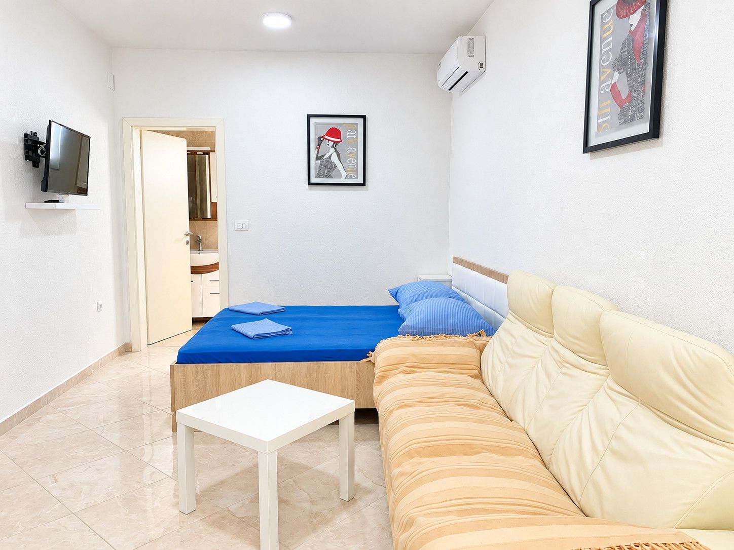 Un dormitorio con cama, sofá, una mesita, televisor y aire acondicionado.