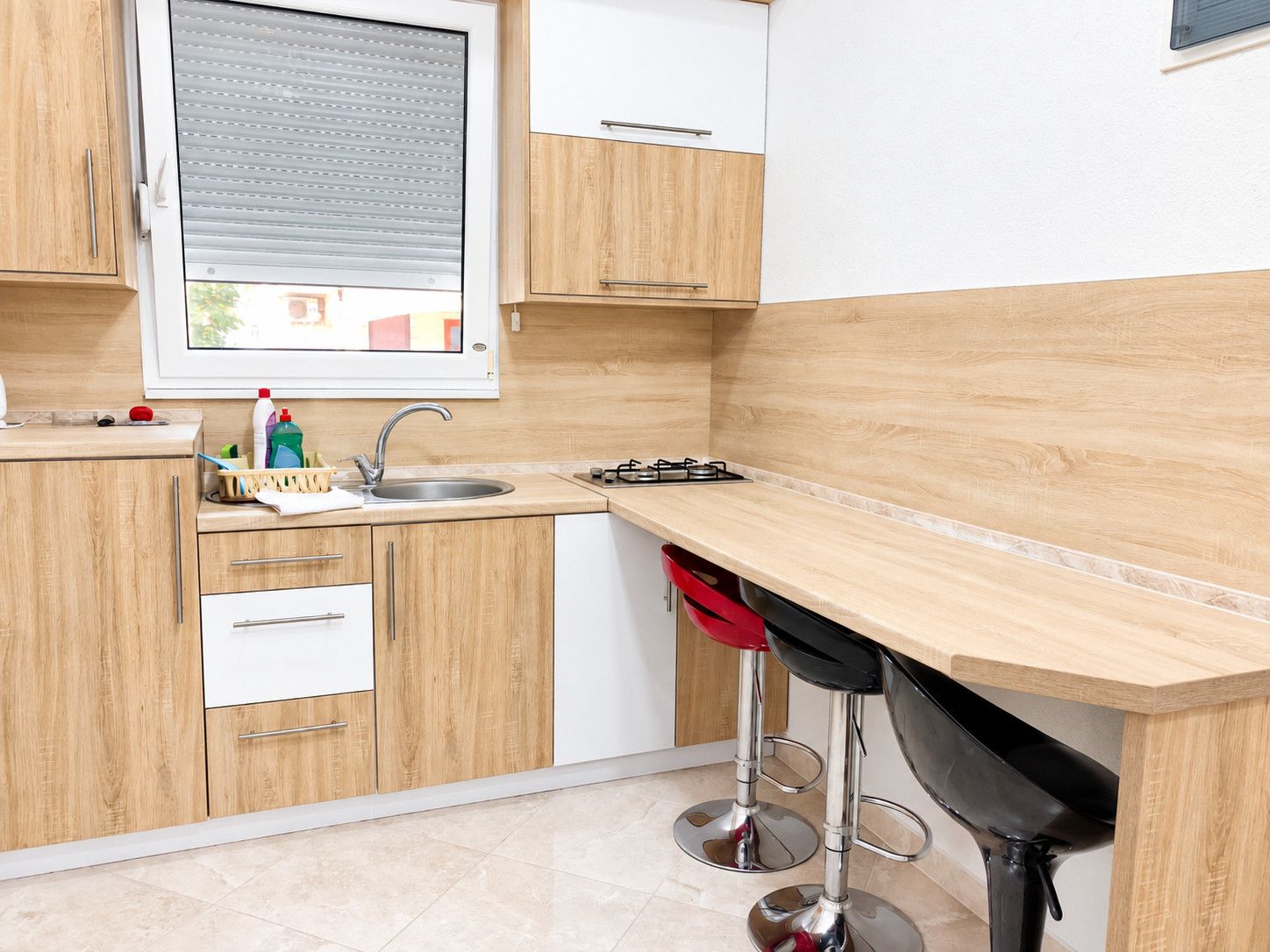 A kitchen with wooden cabinets, a stainless steel sink, a gas stove, and a window with blinds.