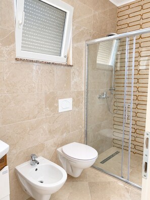Ein Badezimmer mit Duschkabine aus Glas, einem Bidet und einer Toilette.