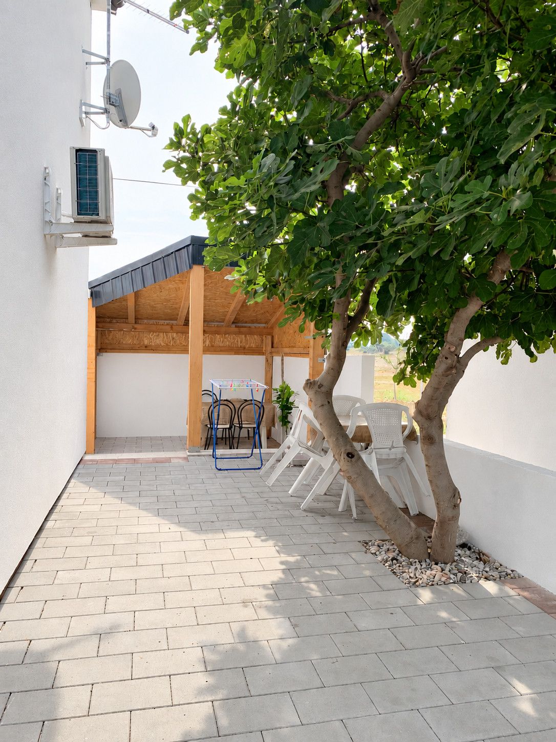 A covered outdoor seating area with a table and chairs, a tree, and a satellite dish on the wall.