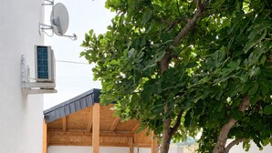 A covered outdoor seating area with a table and chairs, a tree, and a satellite dish on the wall. - Studio Apartment Vir 2 (Vir)