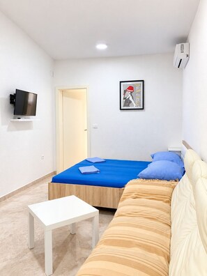Ein Zimmer mit einem Bett, einem Schlafsofa, einem kleinen Tisch, einem Fernseher und einer Tür.
