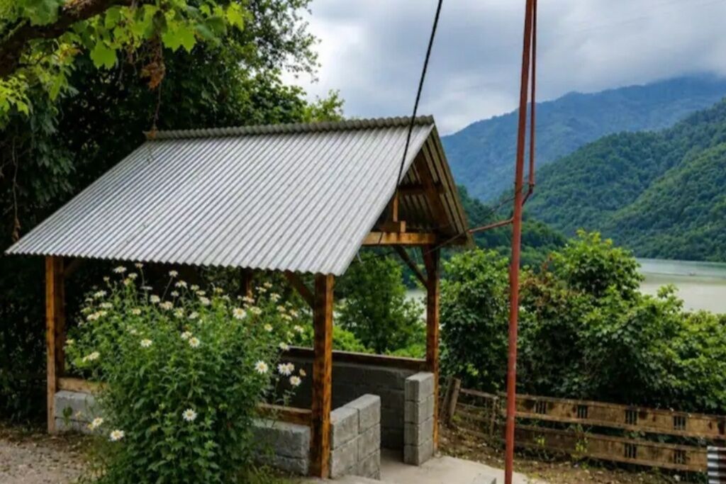Eine kleine Holzhütte mit Wellblechdach, umgeben von üppigem Grün und einer Berglandschaft im Hintergrund.