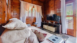 Una camera in una baita di legno con un letto, una televisione, una ventola e un tavolino.