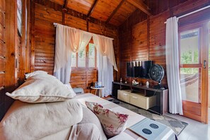 Ein Zimmer in einer Holzhütte mit einem Bett, einem Fernseher, einem Ventilator und einem kleinen Tisch.
