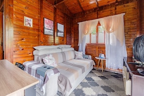 Ein gemütliches Blockhaus mit Holzinnenausstattung, einer Couch mit Kissen, einem kleinen Tisch und einem Ventilator.